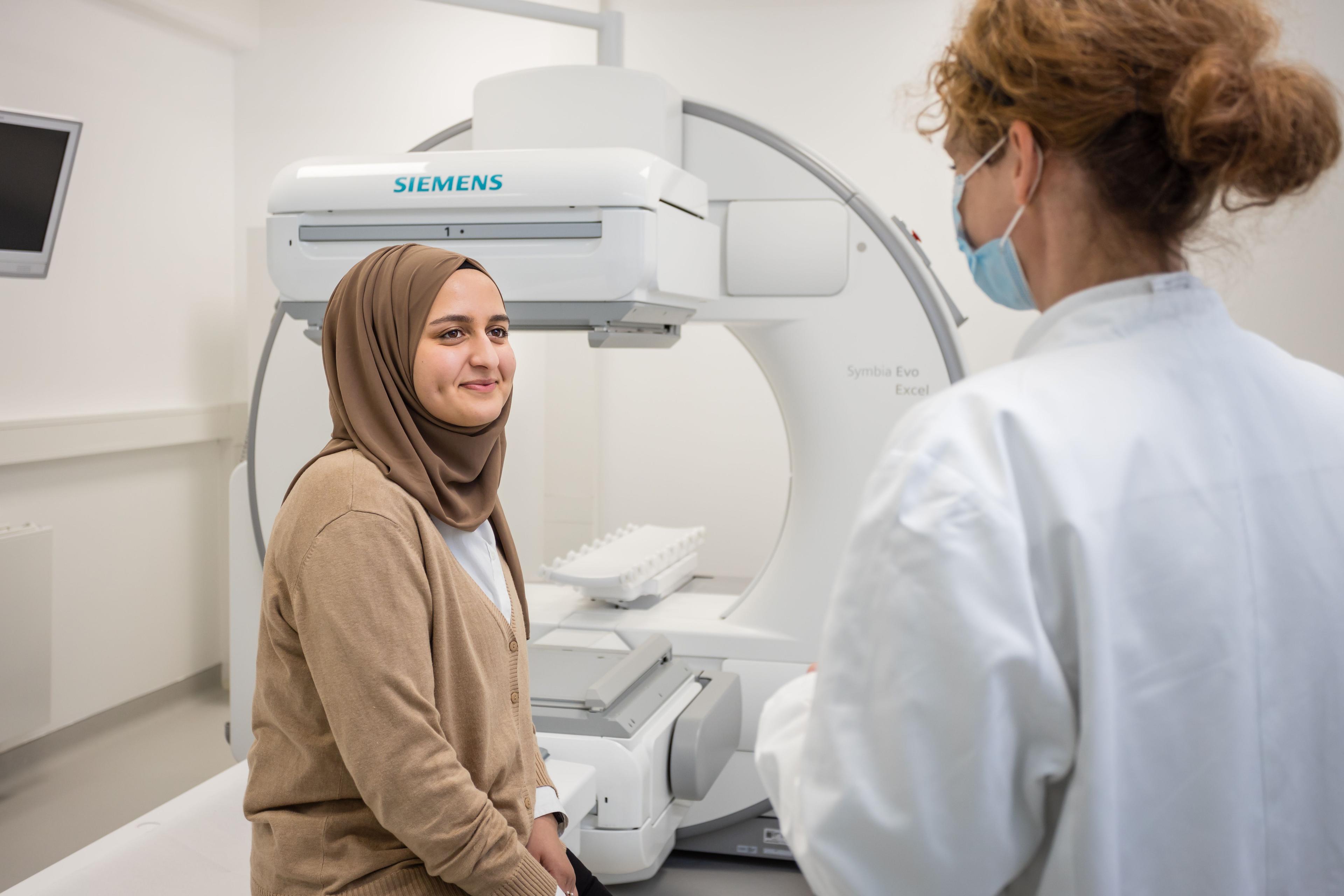 Eine Ärztin erklärt einer Patientin die nuklearmedizinische Untersuchung. Die Patientin sitzt auf der Liege einer Gammakamera..