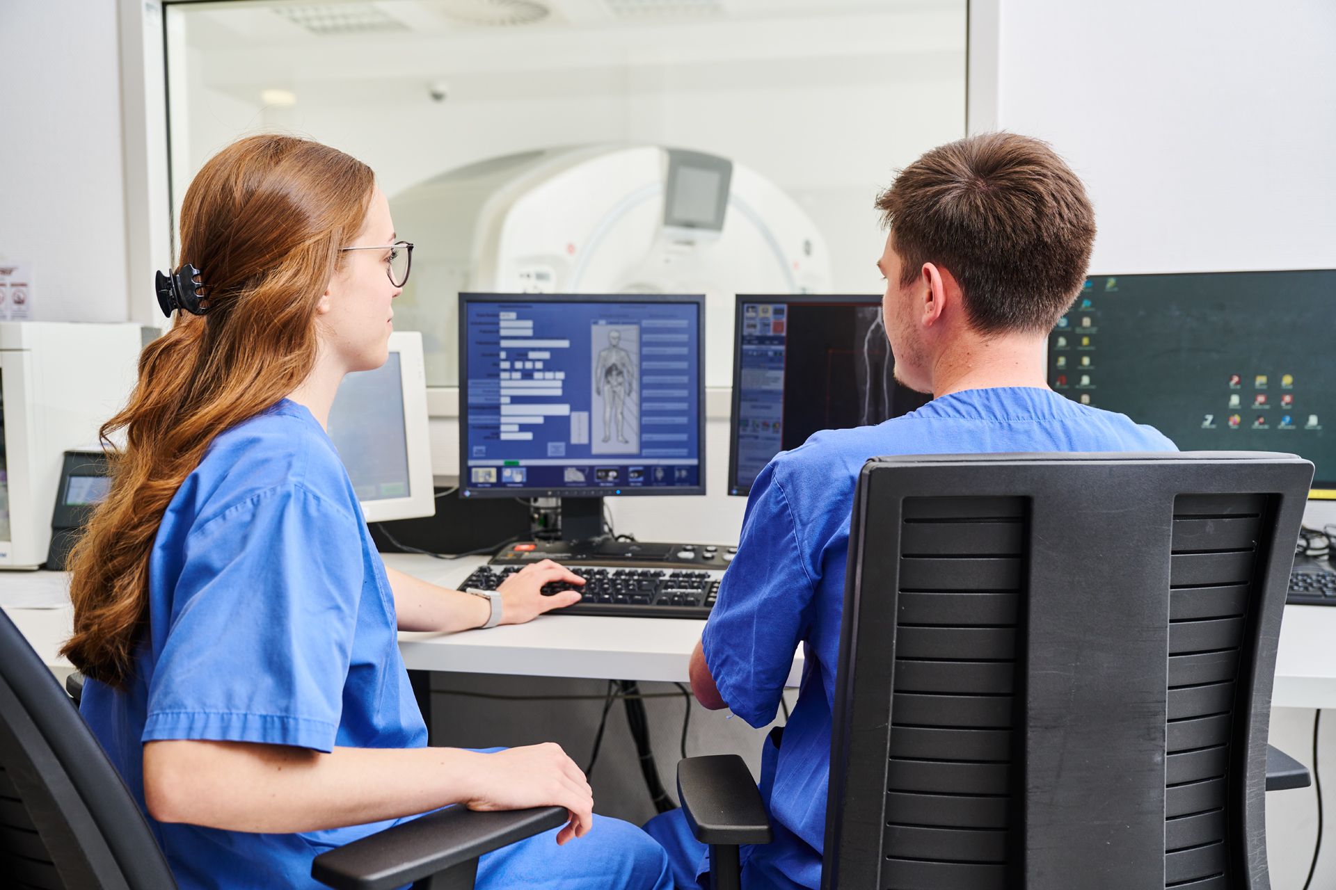 Zwei Medizinische Fachkräfte sitzen an einem Schreibtisch und sehen sich CT-Bilder auf einem Computer Bildschirm an.