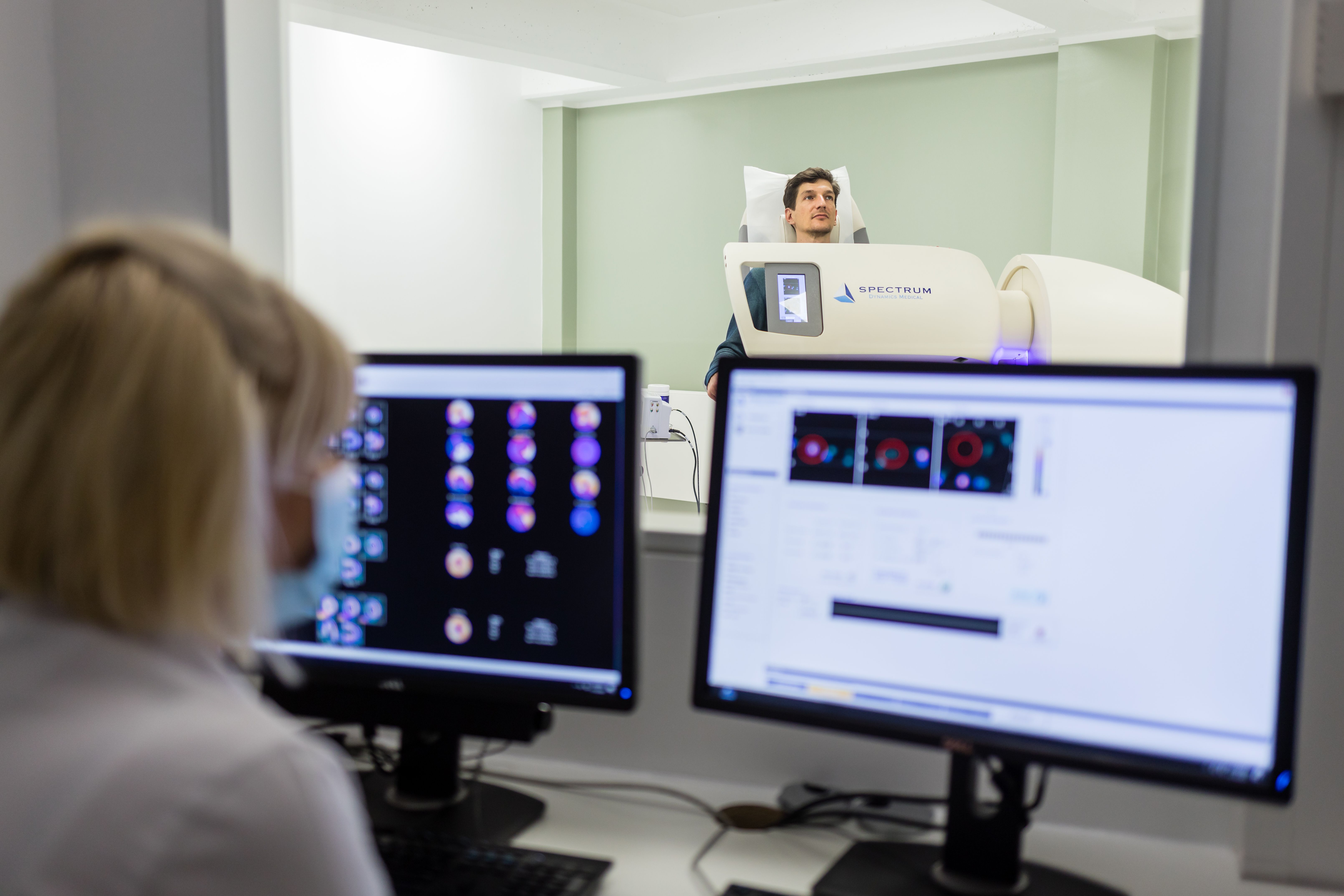Eine Medizinische Fachkraft beaufsichtigt aus dem Vorraum einen Patienten bei einer Myokardszintigraphie im Strahleninstitut Köln.